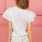 Woman wearing white scallop edged lace trim top with intricate lace detailing, paired with frayed hem shorts, standing against a pink background