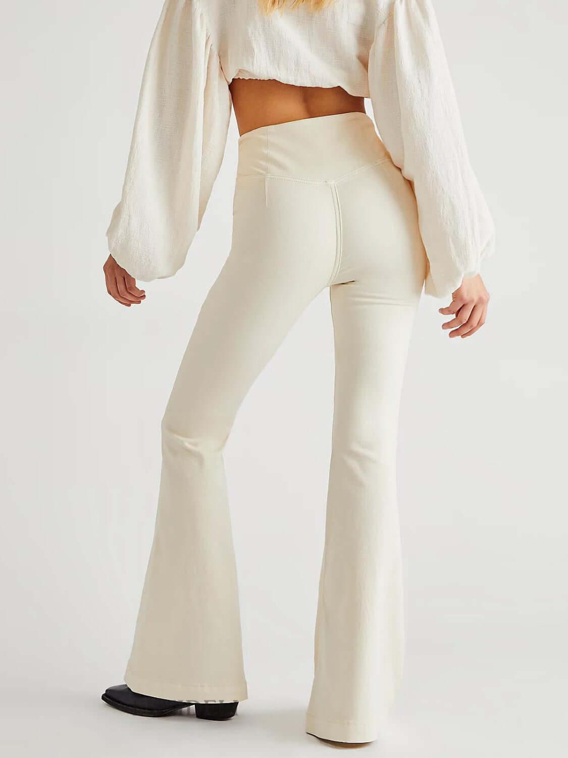 Woman wearing white asymmetric waist flare jeans with a slight stretch and a unique design, showcasing a trendy fashionable look from behind