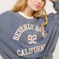 Woman wearing Beverly Hills 92 California contrast crop sweatshirt, showcasing casual style with bold graphic design and cozy comfort.