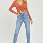 Woman wearing High Rise Frayed Hem Skinny Jeans by Risen Jeans, paired with an orange twist-front top and heels, showcasing trendy style.