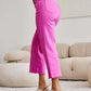 Woman wearing pink RFM Jeans featuring high waist and raw hem while standing in a stylish living room.