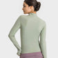 Model showing the back of the Millennia Half Zip Thumbhole Sleeve Sports Top in green, paired with sporty shorts.