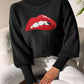 Woman wearing Bella Road Lip Turtleneck Long Sleeve Sweater in black with red lip graphic, sitting on a chair.