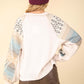 Back view of woman wearing a printed long sleeve round neck knit top with exposed seams and no stretch, paired with a maroon beanie and leather shorts.