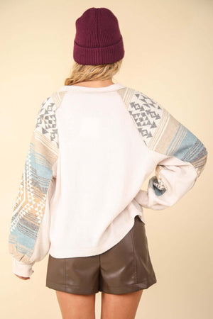 Back view of woman wearing a printed long sleeve round neck knit top with exposed seams and no stretch, paired with a maroon beanie and leather shorts.