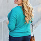 Woman wearing a turquoise Round Neck Batwing Sleeve Top with jeans and sunglasses, carrying a brown purse, standing outdoors.