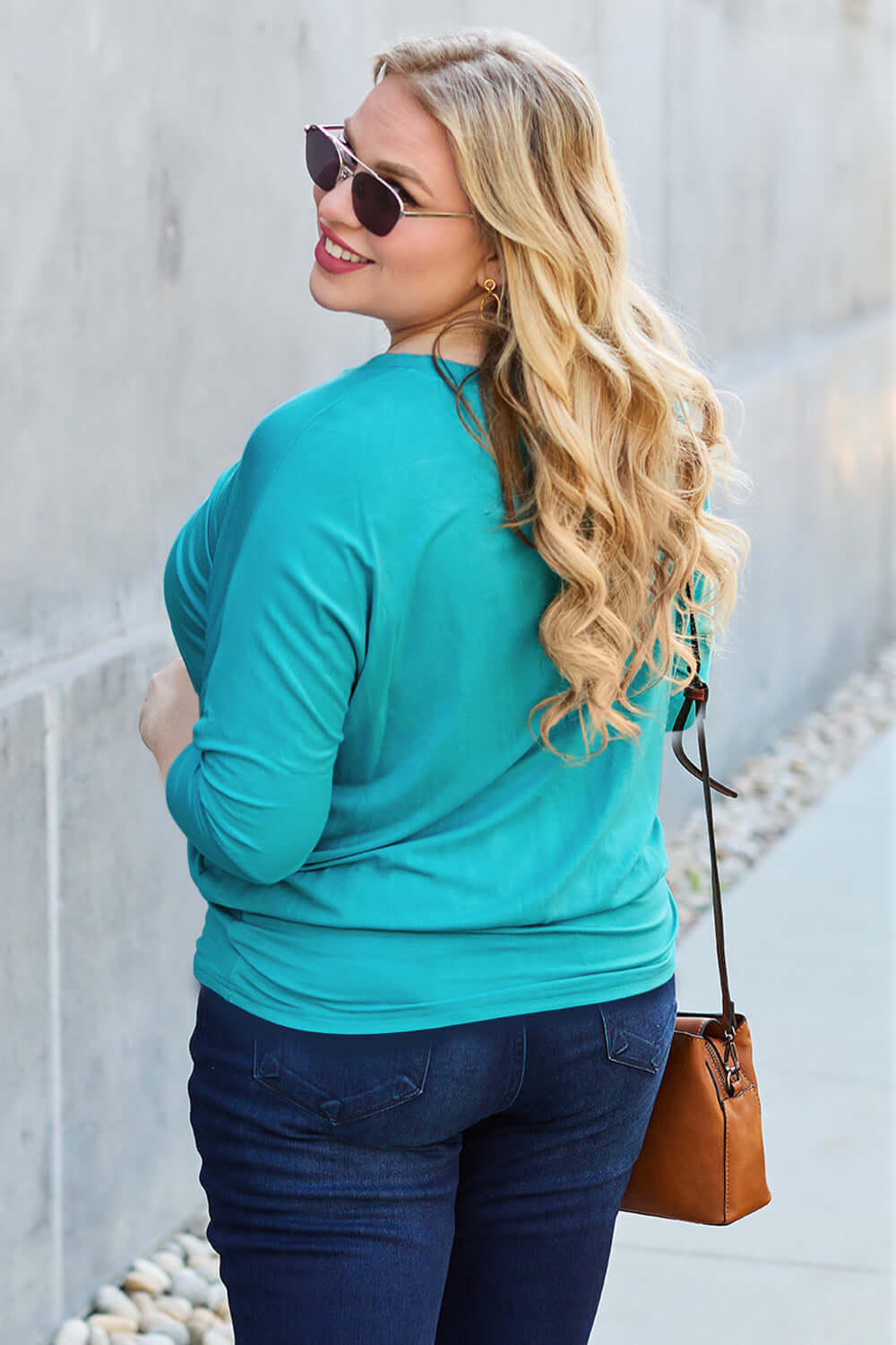 Woman wearing a turquoise Round Neck Batwing Sleeve Top with jeans and sunglasses, carrying a brown purse, standing outdoors.