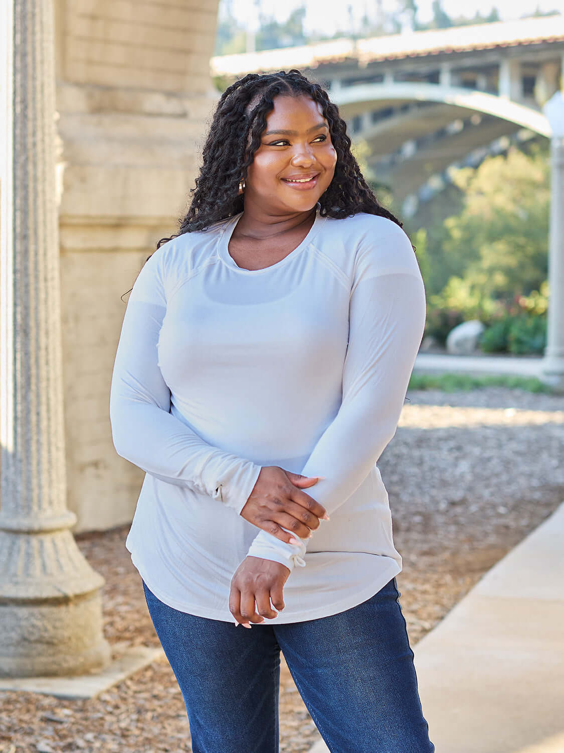 Plus-size woman wearing round neck long sleeve t-shirt paired with jeans, smiling outdoors in a casual setting.