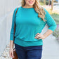 Woman wearing teal round neck batwing sleeve top with jeans, walking outdoors on a sunny day