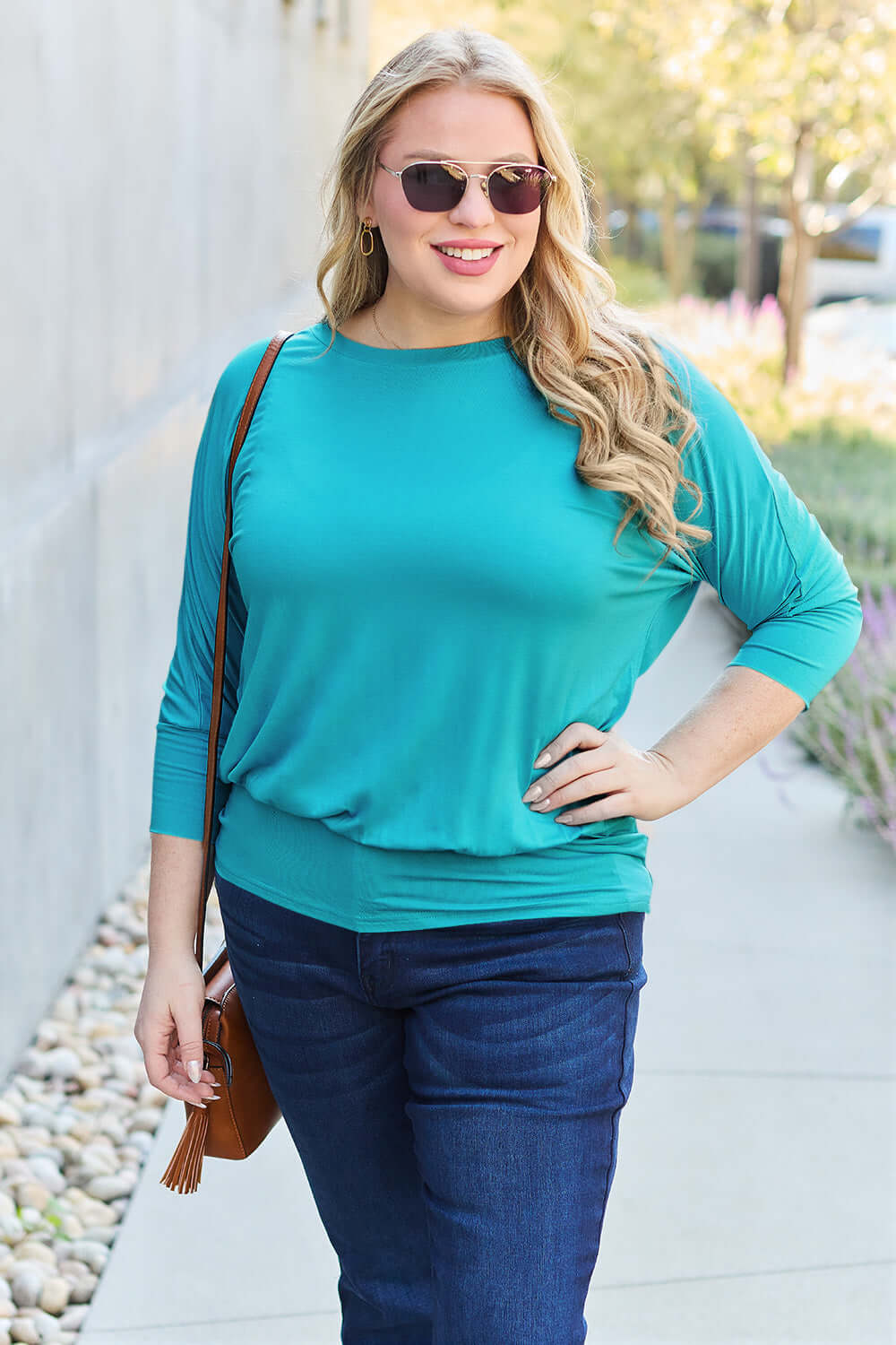 Woman wearing teal round neck batwing sleeve top with jeans, walking outdoors on a sunny day