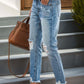 Woman wearing distressed raw hem jeans with pockets, paired with a blue top and heels, standing on stairs carrying a brown handbag