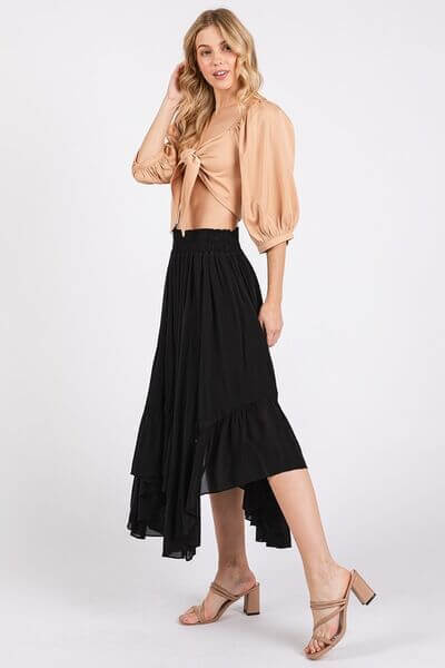 Stylish woman in a handkerchief hem black midi skirt with pockets and a beige tied blouse, showcasing a chic outfit.