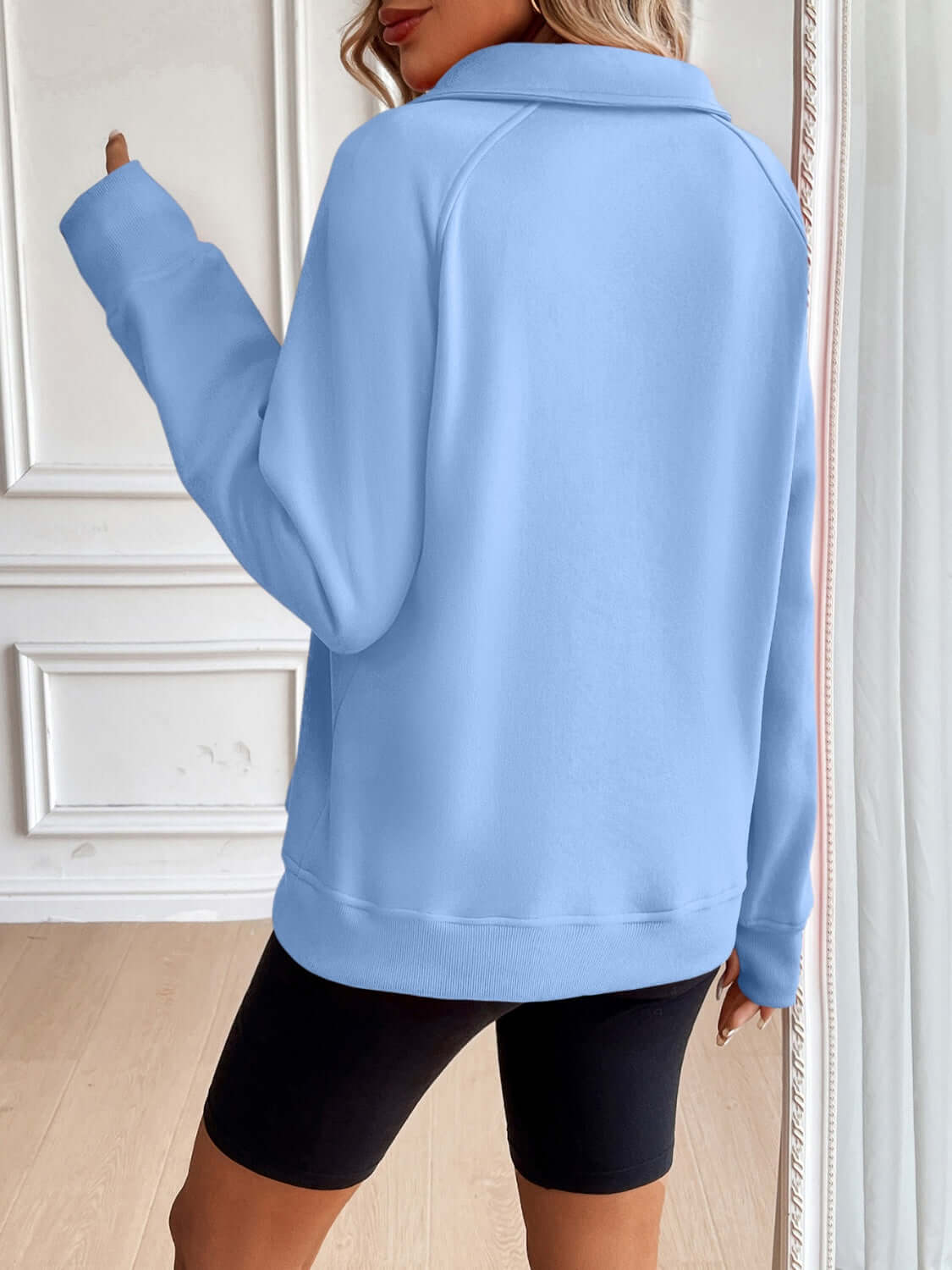 Back view of woman wearing Ivy Lane Half Zip Raglan Sleeve Sweatshirt in blue, showing pocket details and relaxed fit