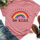 Pink graphic round neck short sleeve T-shirt with "Be Kind" rainbow print, paired with jeans and sandals on a white background.