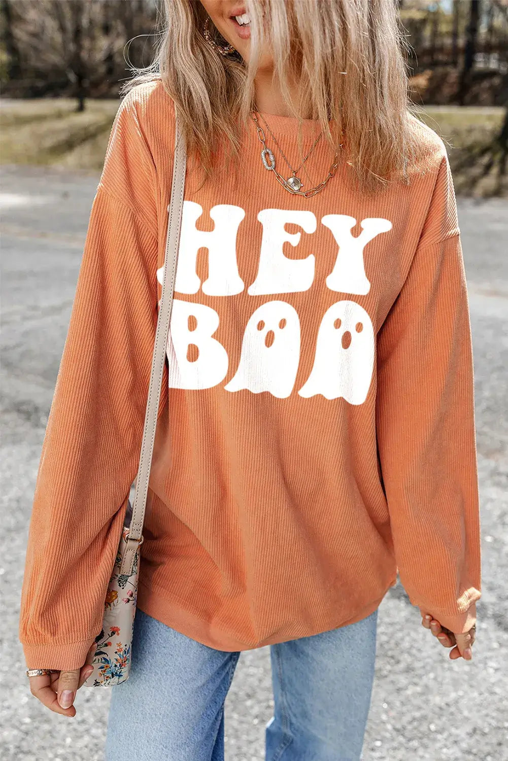 Woman wearing Bella Road Hey Boo Graphic Round Neck Long Sleeve Sweatshirt with "Hey Boo" text and ghost graphics, styled casually outdoors.