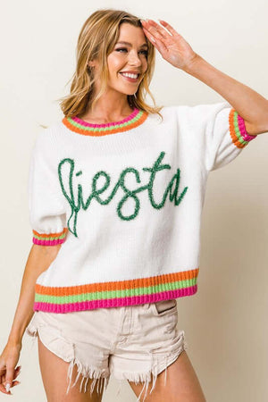 Trendy white sweater with green 'Fiesta' lettering, short puff sleeves, and colorful ribbed trim, perfect for a stylish outfit.