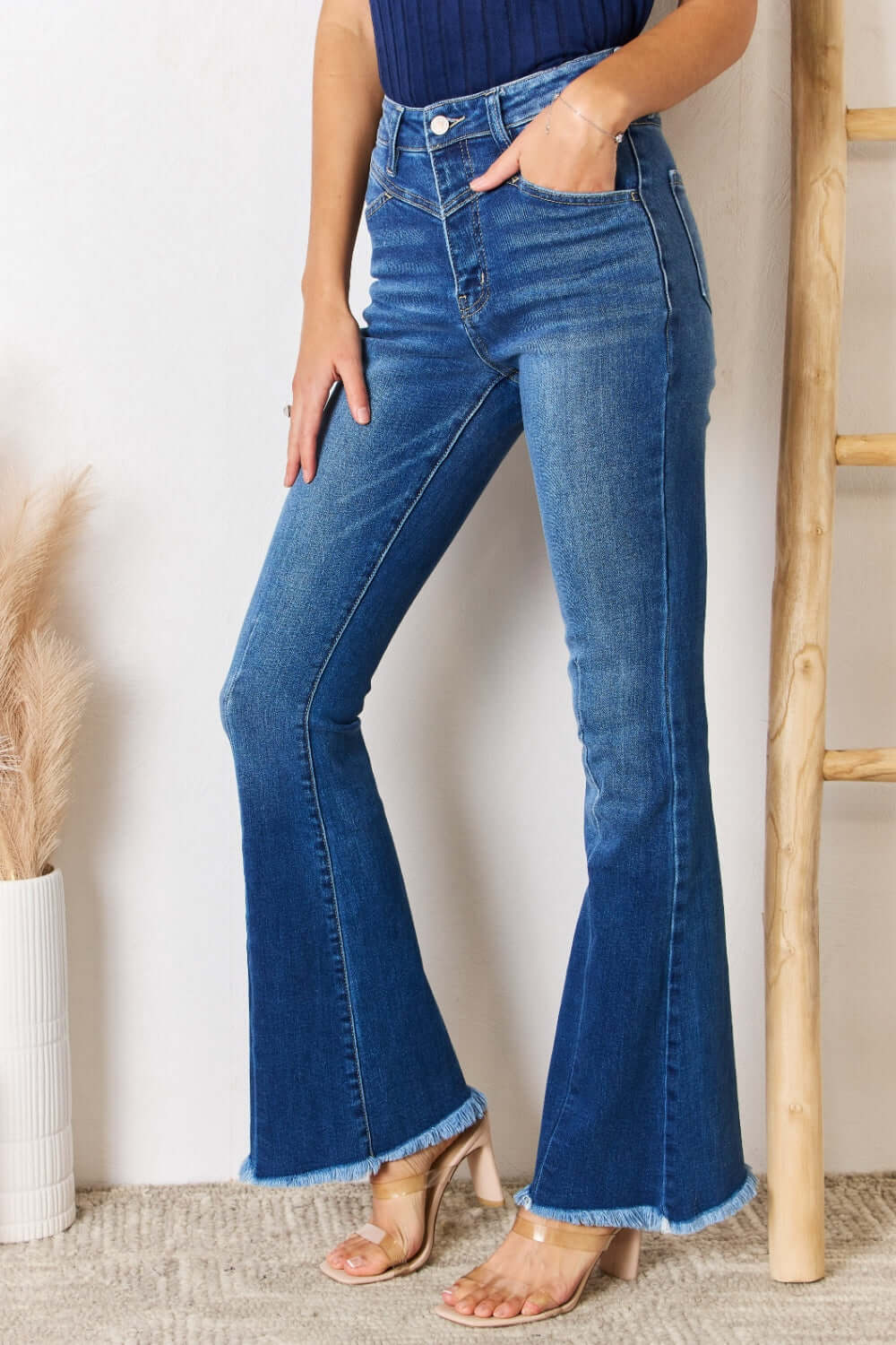 Woman wearing Kancan high rise raw hem flare jeans with front yoke seam and frayed hem for a chic retro look