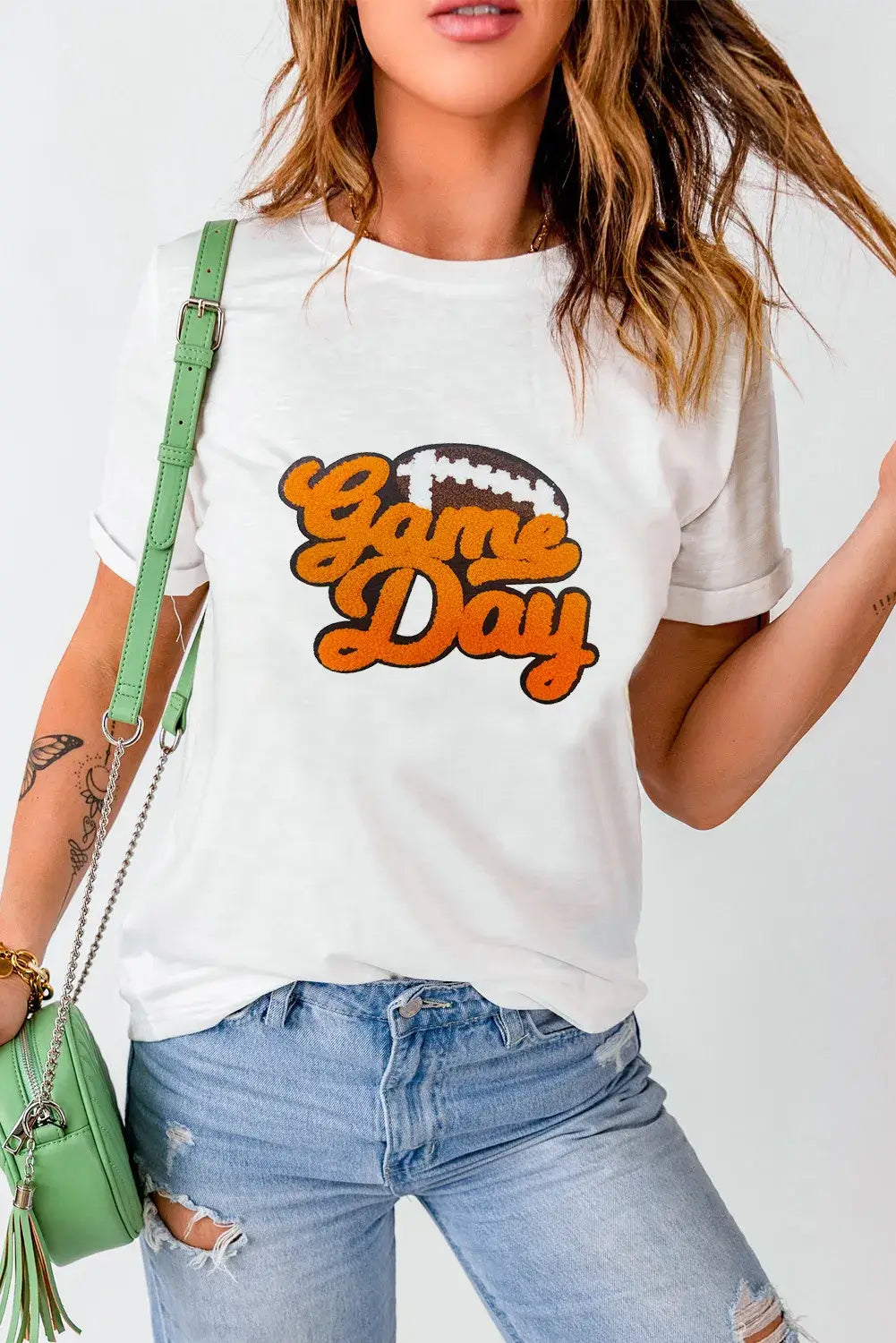 Woman wearing GAME DAY round neck short sleeve t-shirt, white with orange text, paired with distressed jeans and green shoulder bag.