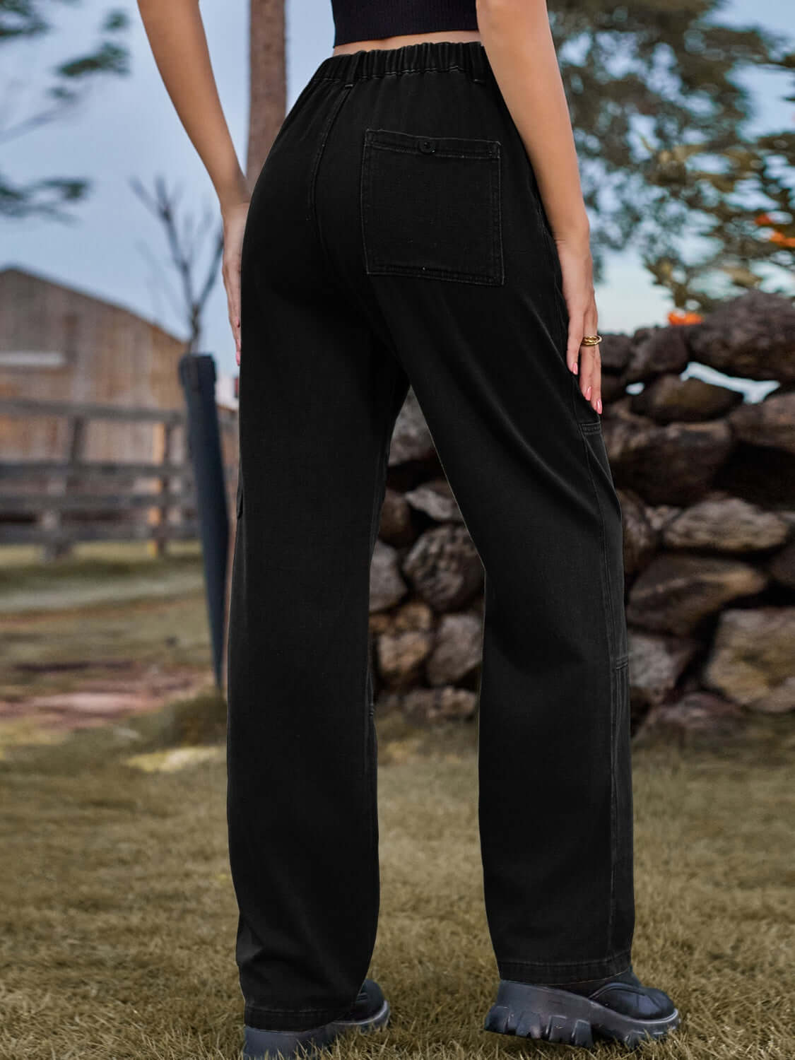 Woman wearing Bella Road high waist cargo straight jeans in black with back pocket detailing, standing outside near a stone wall.