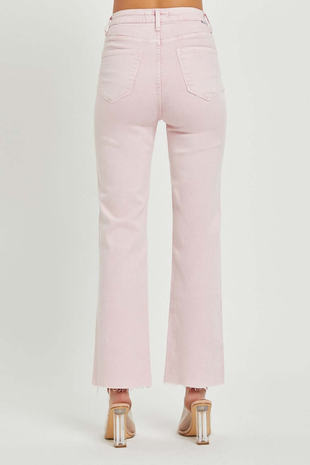 Pink RISEN high rise full size tummy control straight jeans with raw hem detail from the back, paired with clear heels.