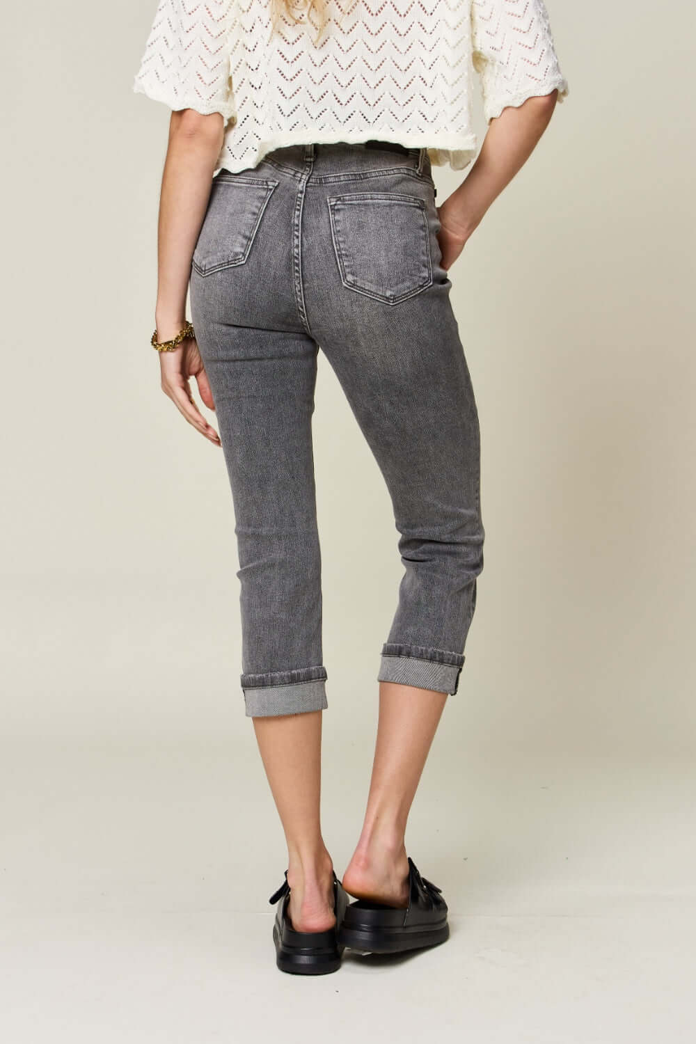 Woman wearing Button Fly High Waist Cuffed Capris in gray by Judy Blue Jeans, showcasing back view with chic casual style.