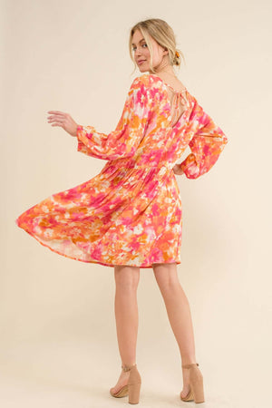 Woman modeling a full-size printed tie-back long sleeve dress with an intricate design, showcasing its elegant fit and vibrant colors.