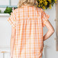 Woman wearing an orange plaid button-up short sleeve shirt, showing back view in cozy indoor setting.