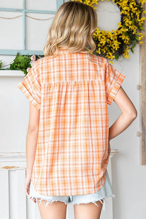 Woman wearing an orange plaid button-up short sleeve shirt, showing back view in cozy indoor setting.