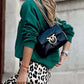 Woman in green Bella Road 'Dreamer' sweatshirt with black bag and leopard skirt, exuding style and comfort.