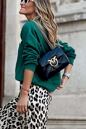 Woman in green Bella Road 'Dreamer' sweatshirt with black bag and leopard skirt, exuding style and comfort.