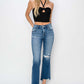 Stylish woman wearing Risen Jeans frayed step hem ankle straight jeans with a black crop top and heels, front view.