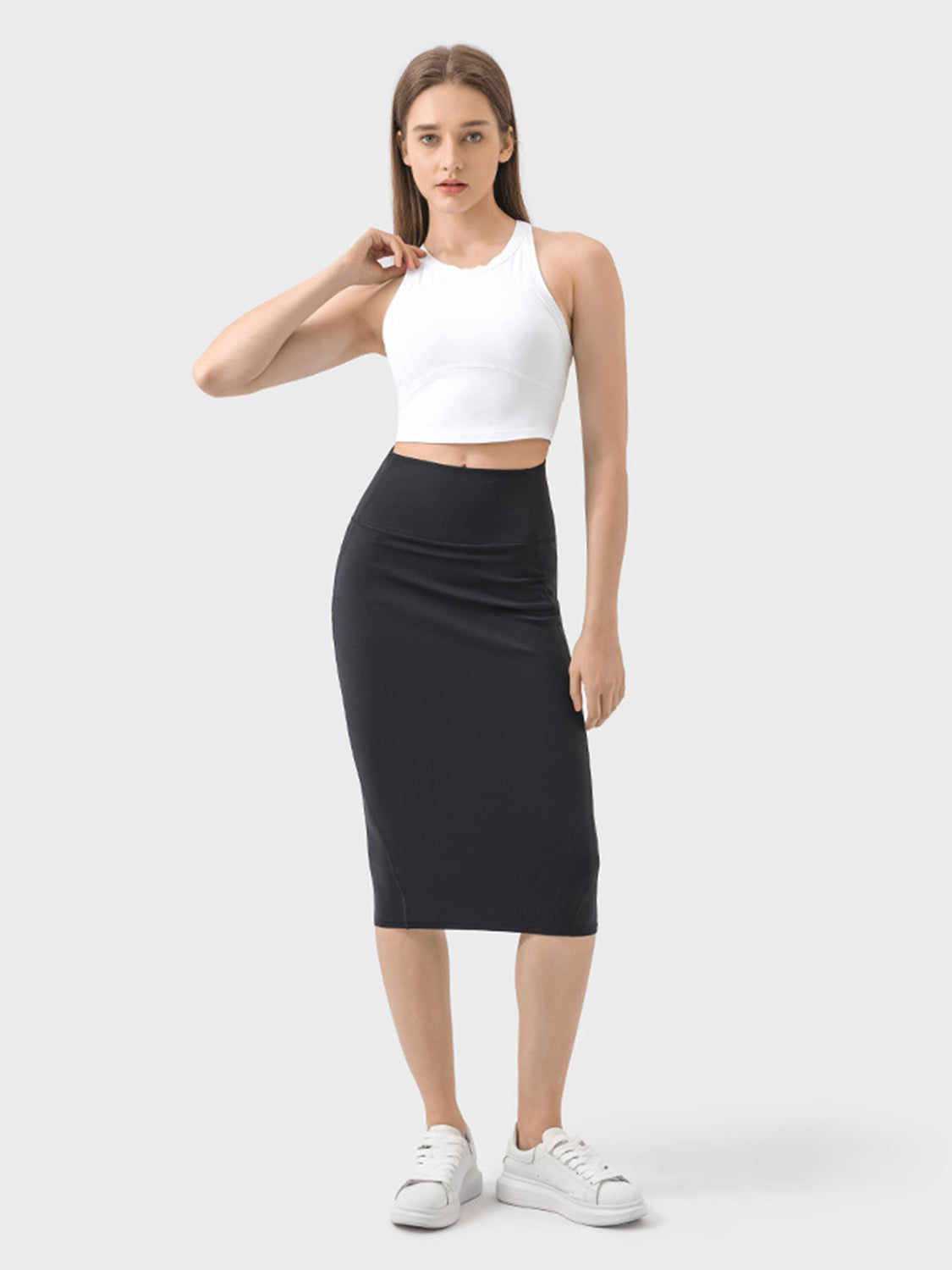 Model showcasing the Millennia Slit Wrap Active Skirt with a white crop top and stylish sneakers in a minimalistic setting.