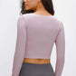 Woman wearing a lilac long-sleeve cropped top with a sports strap, showcasing the back view. Perfect for medium/high impact activities.