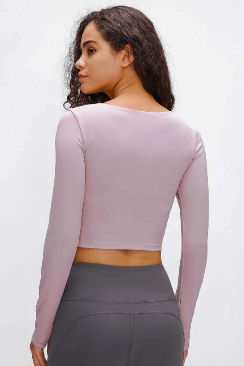 Woman wearing a lilac long-sleeve cropped top with a sports strap, showcasing the back view. Perfect for medium/high impact activities.