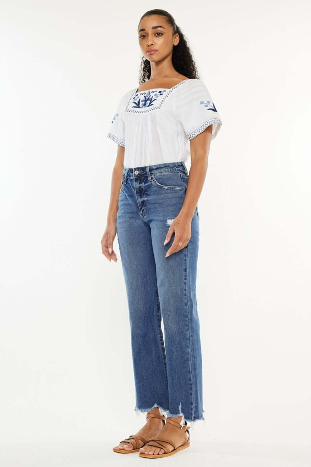 Woman wearing Kancan Full Size High Rise Slim Wide Leg Jeans in a medium wash, paired with a white embroidered top.