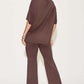 Woman wearing a brown bamboo drop shoulder T-shirt and flare pants set, viewed from the back, showcasing the two-piece outfit's relaxed fit and basic style.