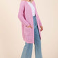 Stylish woman in a pink open front longline cardigan paired with flared jeans, perfect for layering and versatile fashion.