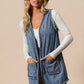 Stylish woman in a BiBi open front denim vest with pockets, paired with a hat against a neutral background.