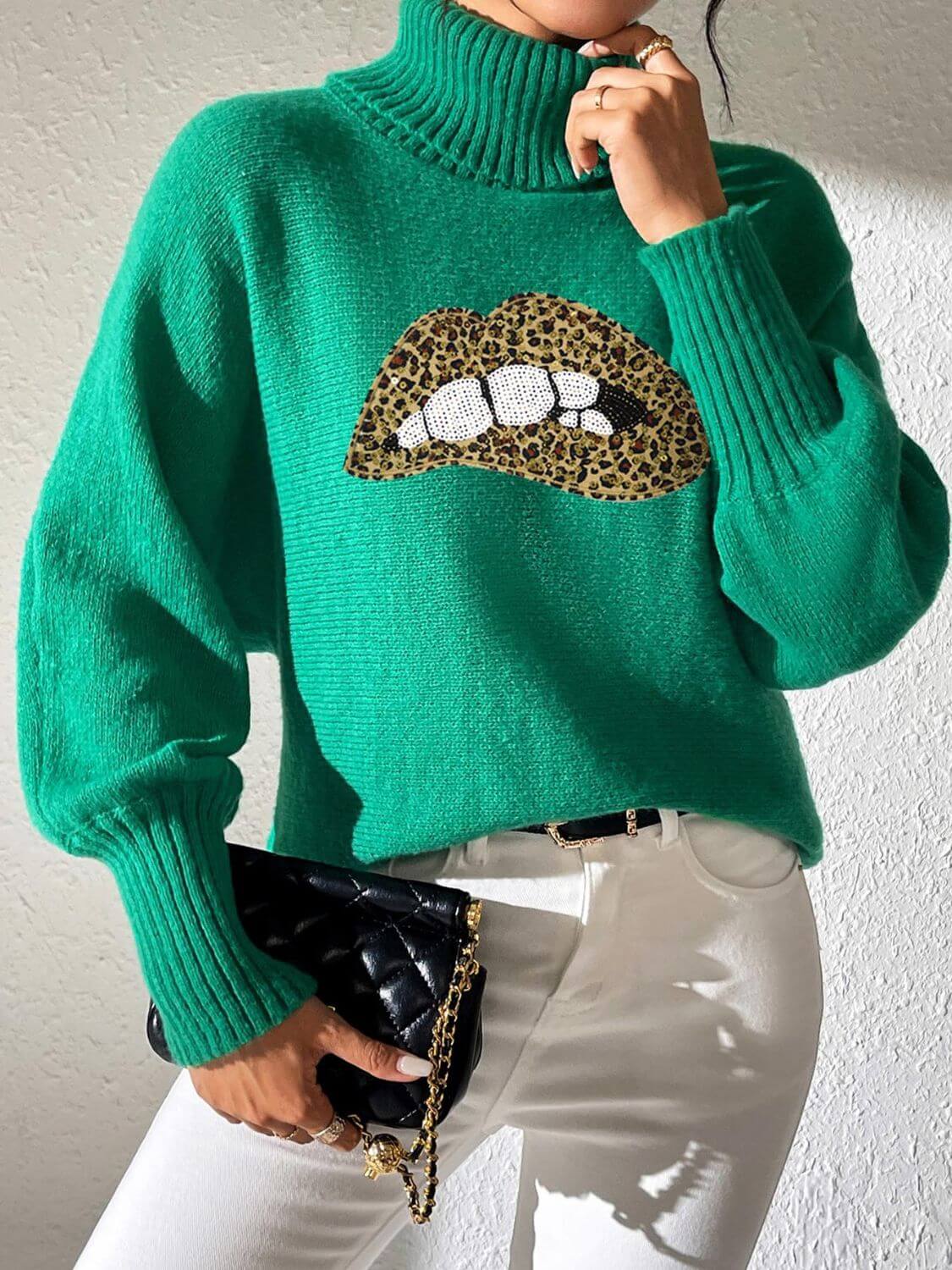 Green Bella Road Lip Turtleneck Sweater with playful design, paired with white pants and clutch.