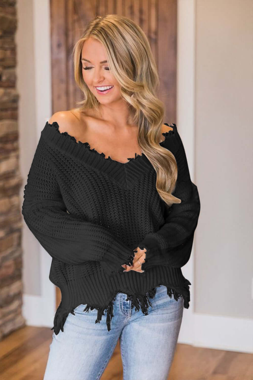 Woman wearing Bella Road black frayed hem dropped shoulder sweater with jeans, exuding playful and stylish vibes.