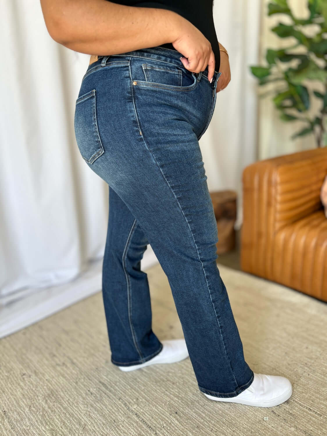 High rise straight leg jeans with tummy control in dark wash, modeled by a woman standing in a stylish living room setting.