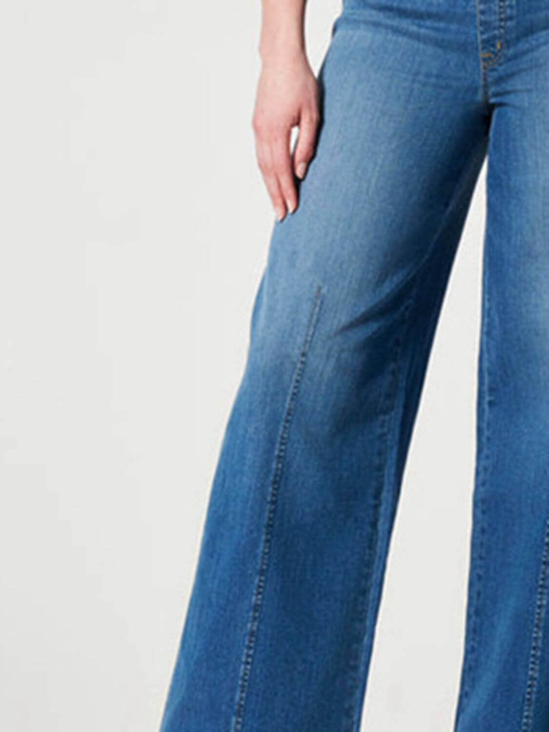 Woman wearing chic wide leg long jeans in solid blue denim with moderate stretch, ideal for a casual yet stylish look.