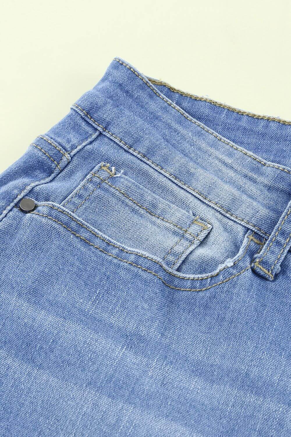 Close-up of Bella Road Button-Fly Distressed Raw Hem Flare Jeans in light blue denim showing back pocket and seam details.