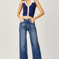 Model wearing Risen high rise frayed hem wide leg jeans paired with a navy and white sleeveless top