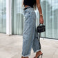 Woman wearing high waist wide leg jeans with black tank top and heels holding a small black purse.