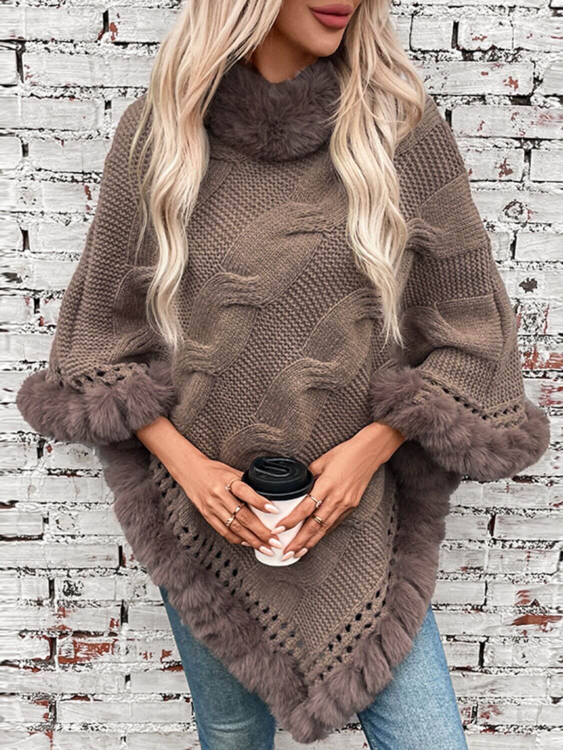 Cozy Bella Road Fuzzy Hem Cable-Knit Poncho in taupe, styled with a coffee cup against a textured brick wall.