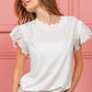 Woman wearing a white scallop edged lace trim top with ruffled sleeves against a pink background, styled with sunglasses and light jeans.