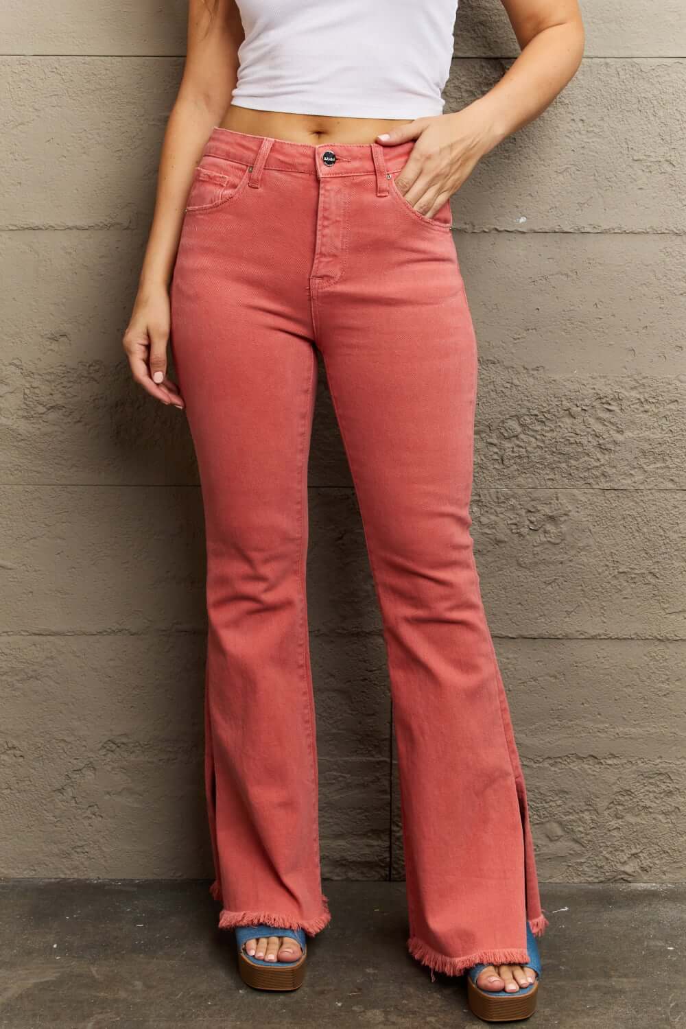 Woman wearing Bailey High Waist Side Slit Flare Jeans in coral, showcasing trendy side slits and a flattering fit. Risen Jeans.