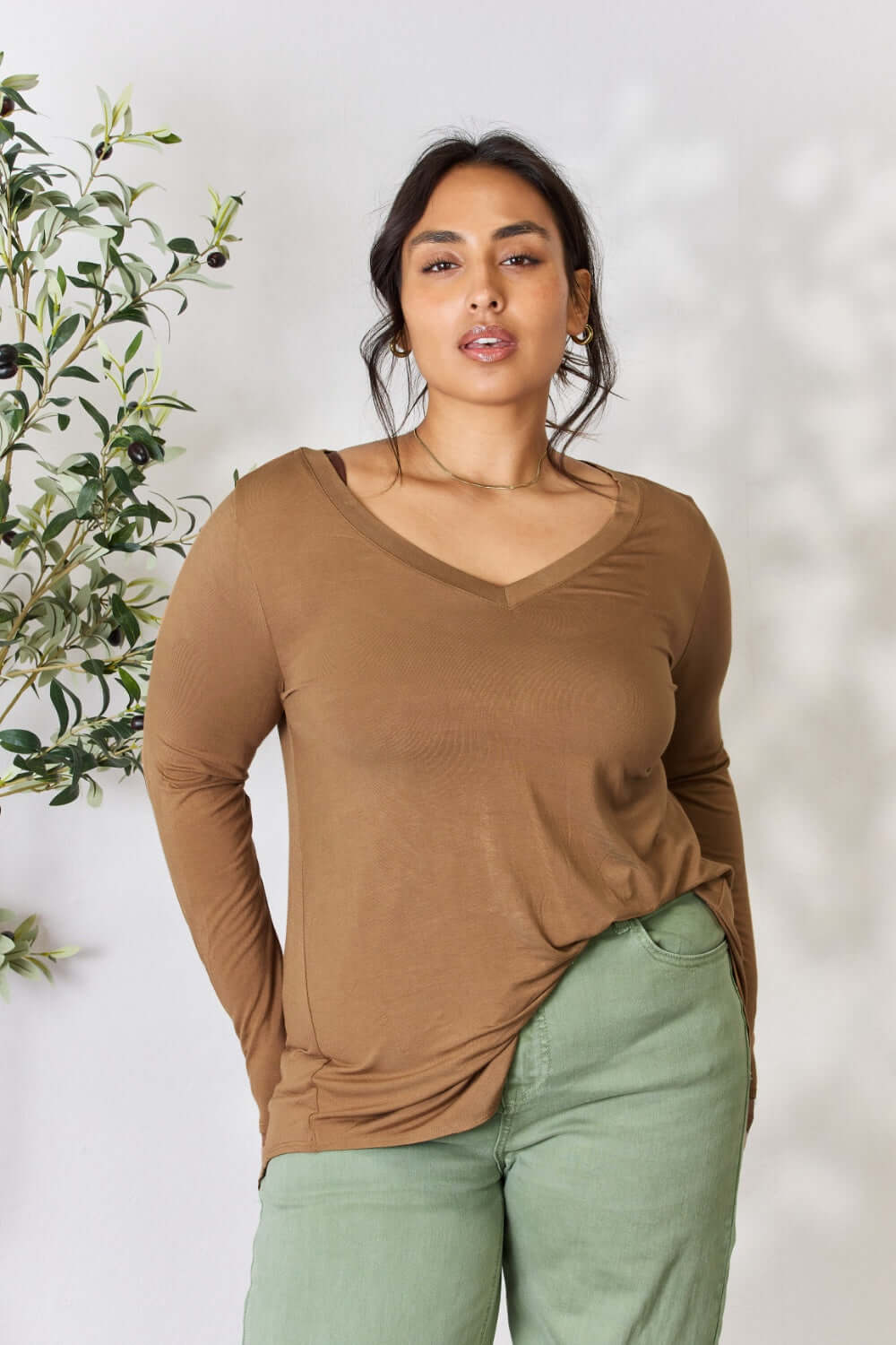 Woman wearing a brown long sleeve V-neck top made of luxurious rayon, paired with green pants, showcasing a flattering and sophisticated look.