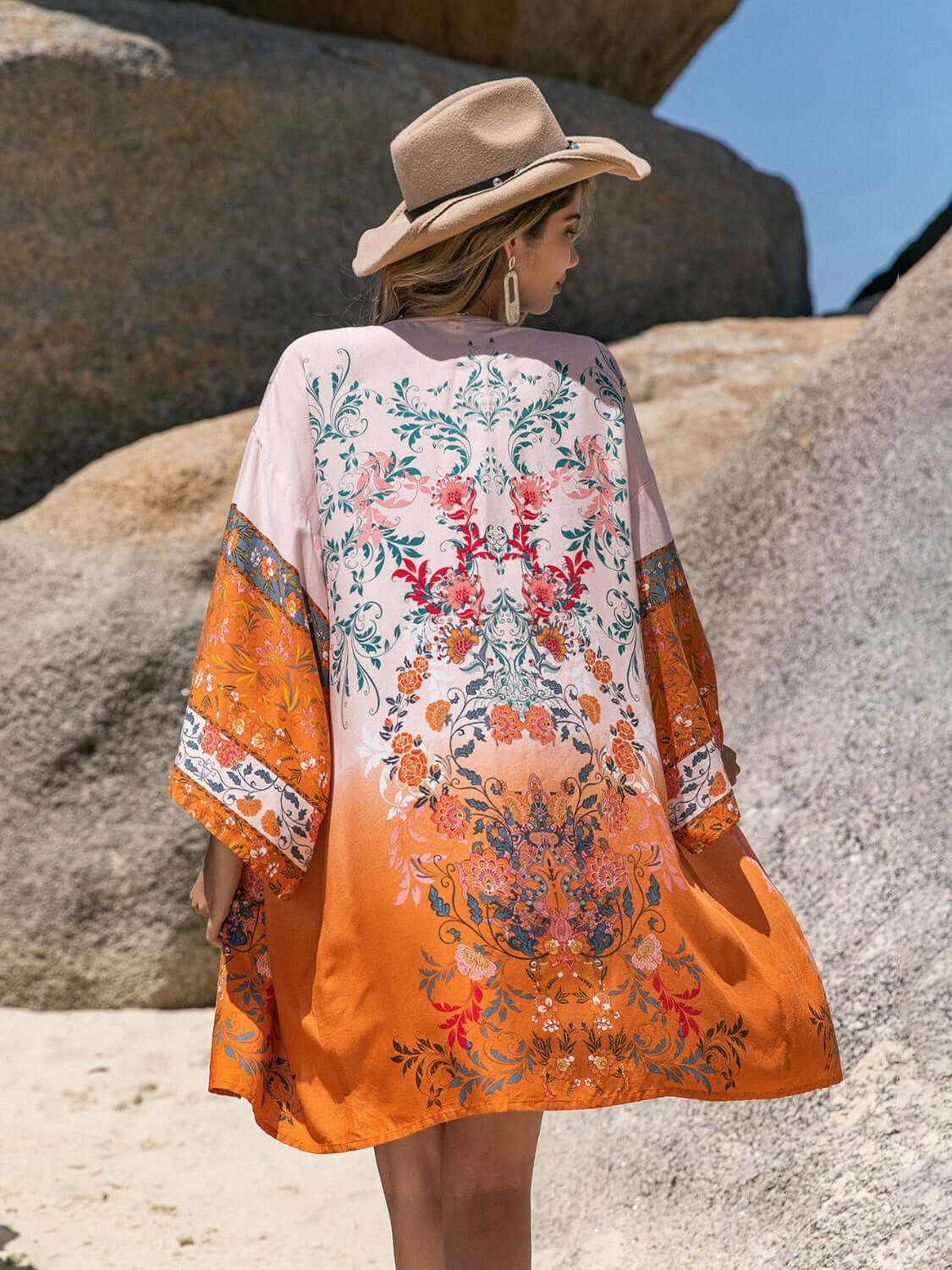 Woman wearing Bella Road Swim printed open front cover-up in vibrant colors at the beach, accessorized with a hat.